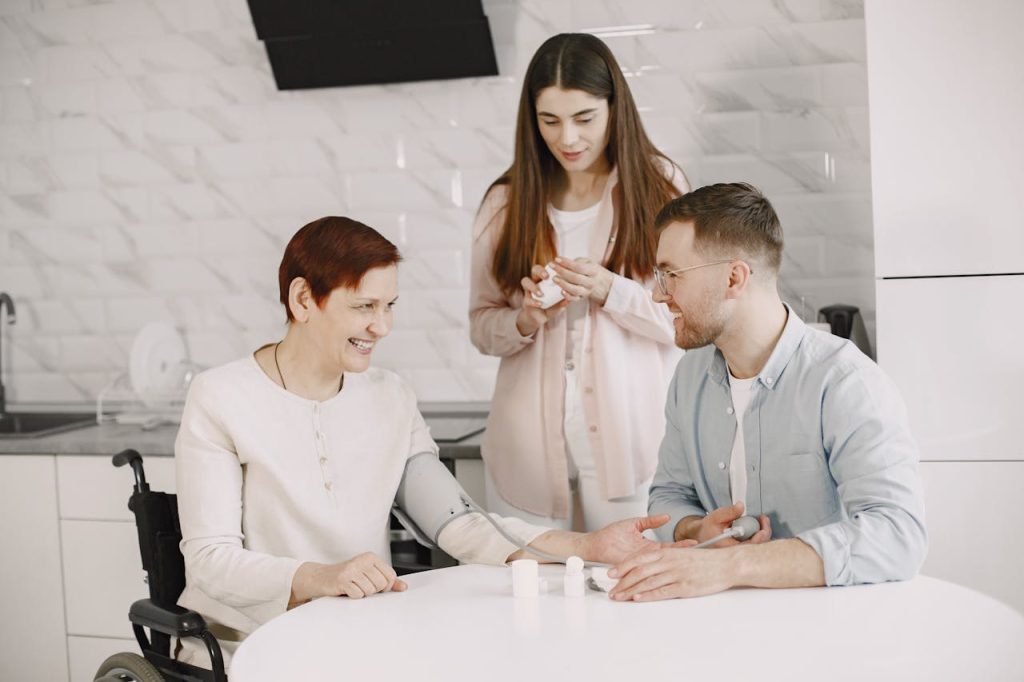 A cozy family moment as an elderly woman has her blood pressure checked by a younger man, with another woman nearby.